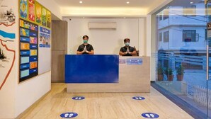 A reception area with a blue counter, two staff members, and a wall with various posters. - The Blue Jay Hostel | Dorms & Rooms (Rishikesh)