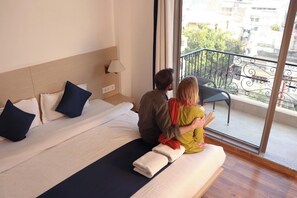 A hotel room with a large bed, a nightstand, a lamp, and a view of the outside balcony.