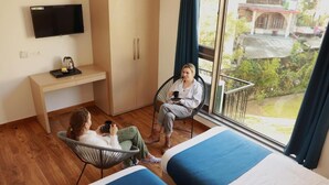 A room with two beds, a desk, a chair, and a TV. - The Blue Jay Hostel | Dorms & Rooms (Rishikesh)