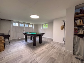 Quarto com mesa de bilhar, piso de madeira, luminária no teto e estante de livros.
