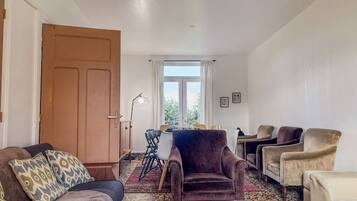 A living room with a sofa, armchairs, a dining table with chairs, a large window, and a door.