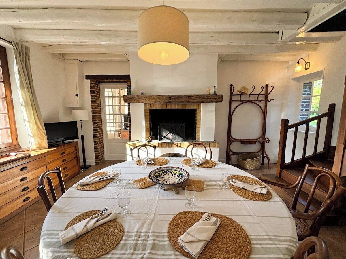 A dining room with a round table set for four, a fireplace, wooden chairs, and a television on a wooden cabinet.