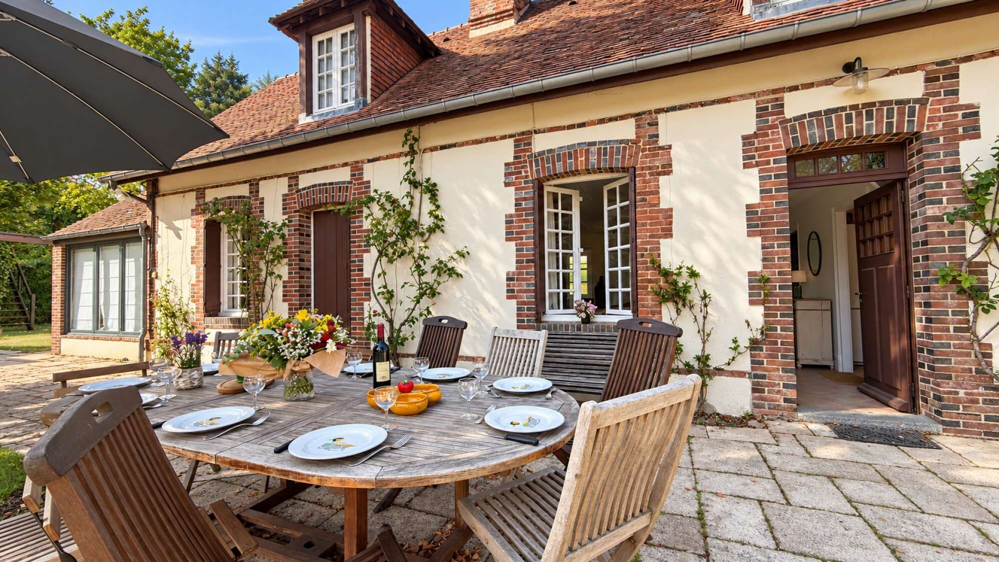 An outdoor dining area with a round wooden table set for four, surrounded by wooden chairs.