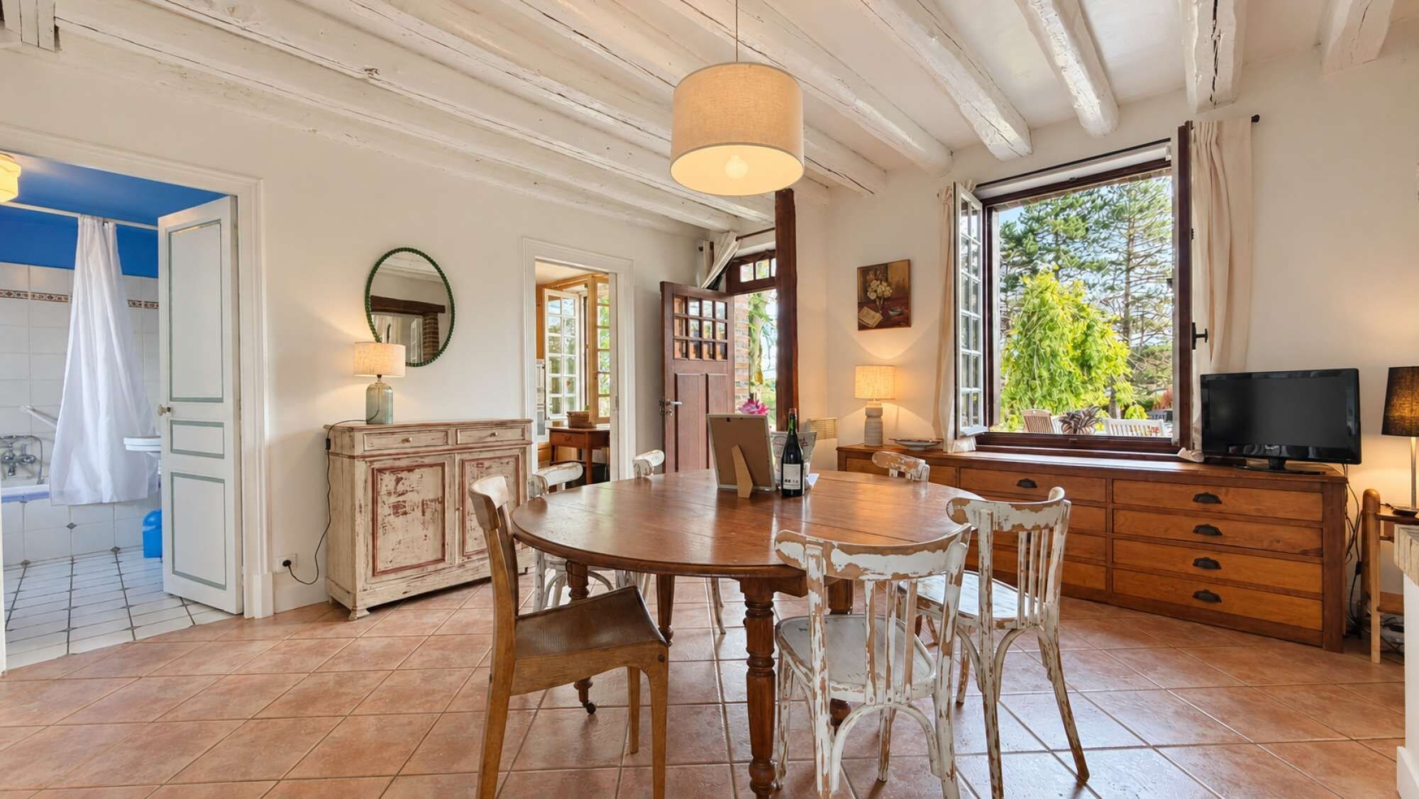Un coin repas avec une table et des chaises en bois, un téléviseur et une fenêtre donnant sur un paysage verdoyant.