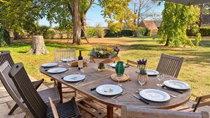 An outdoor dining area with a wooden table set for a meal, surrounded by chairs. - La Maison du Tilleul with a pool for 10 people (Saint-Sulpice-sur-Risle)