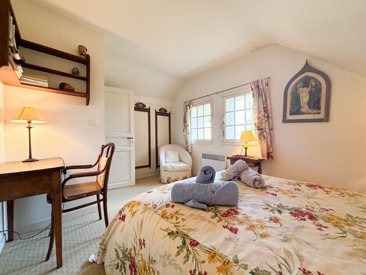 Een slaapkamer met een bloemenbedekker, een bureau met een lamp, een stoel en een bed met opgerolde handdoeken.