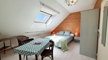 Ett mysigt sovrum på vinden med ett sluttande tak, ett takfönster, en säng med ett grönt överkast, ett litet bord med en rutig duk och en stol.
