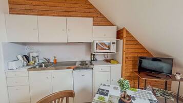 A compact kitchen with white cabinets, a microwave, a coffee maker, and a small TV.