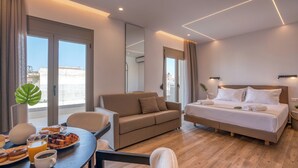 A modern hotel room with a bed, a sofa, a dining table with breakfast, and large windows. - kiwi butique studios (Kissamos)