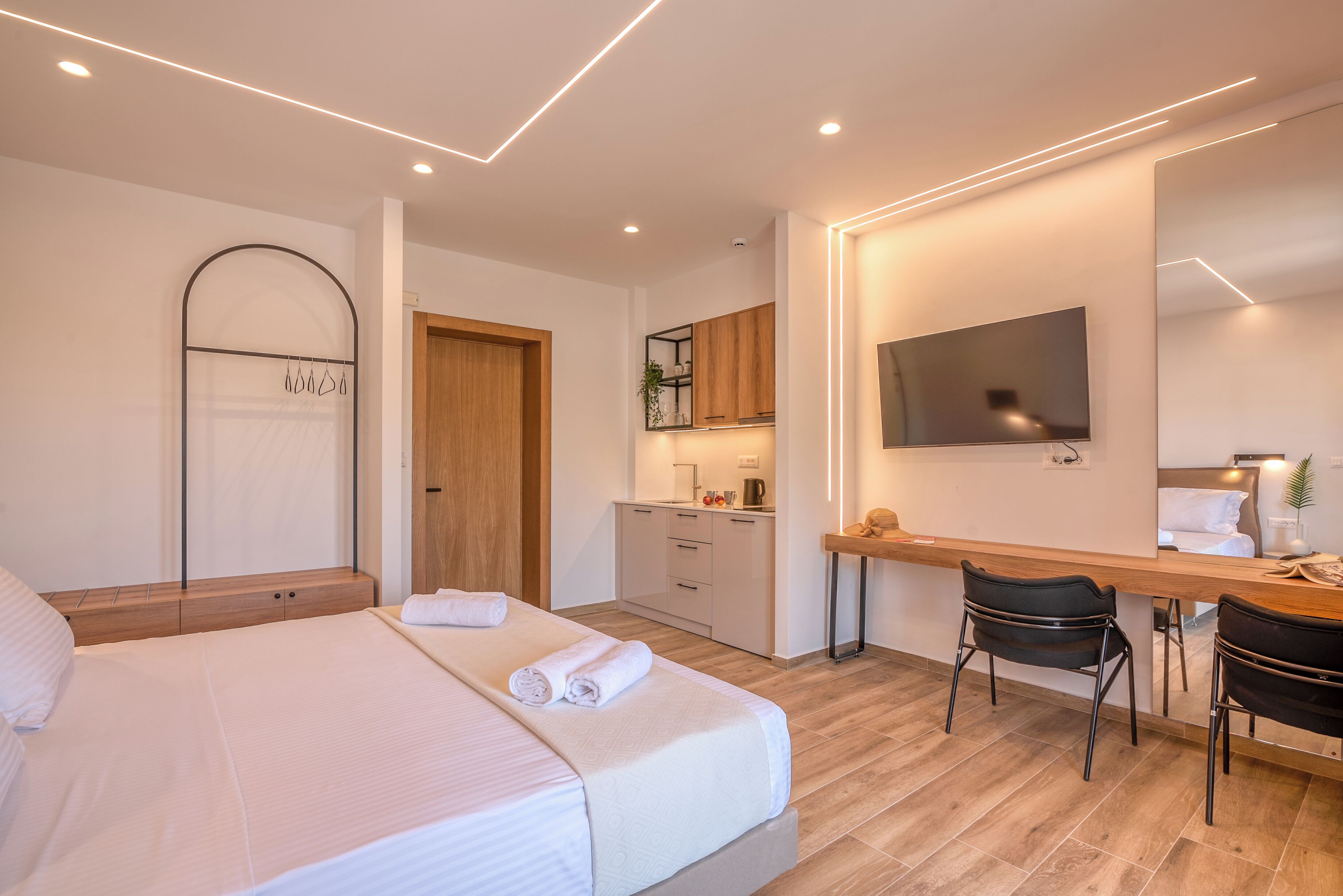 Et moderne hotelværelse med en pænt redt seng, et træskrivebord, en stol, et fjernsyn og et lille tekøkken.