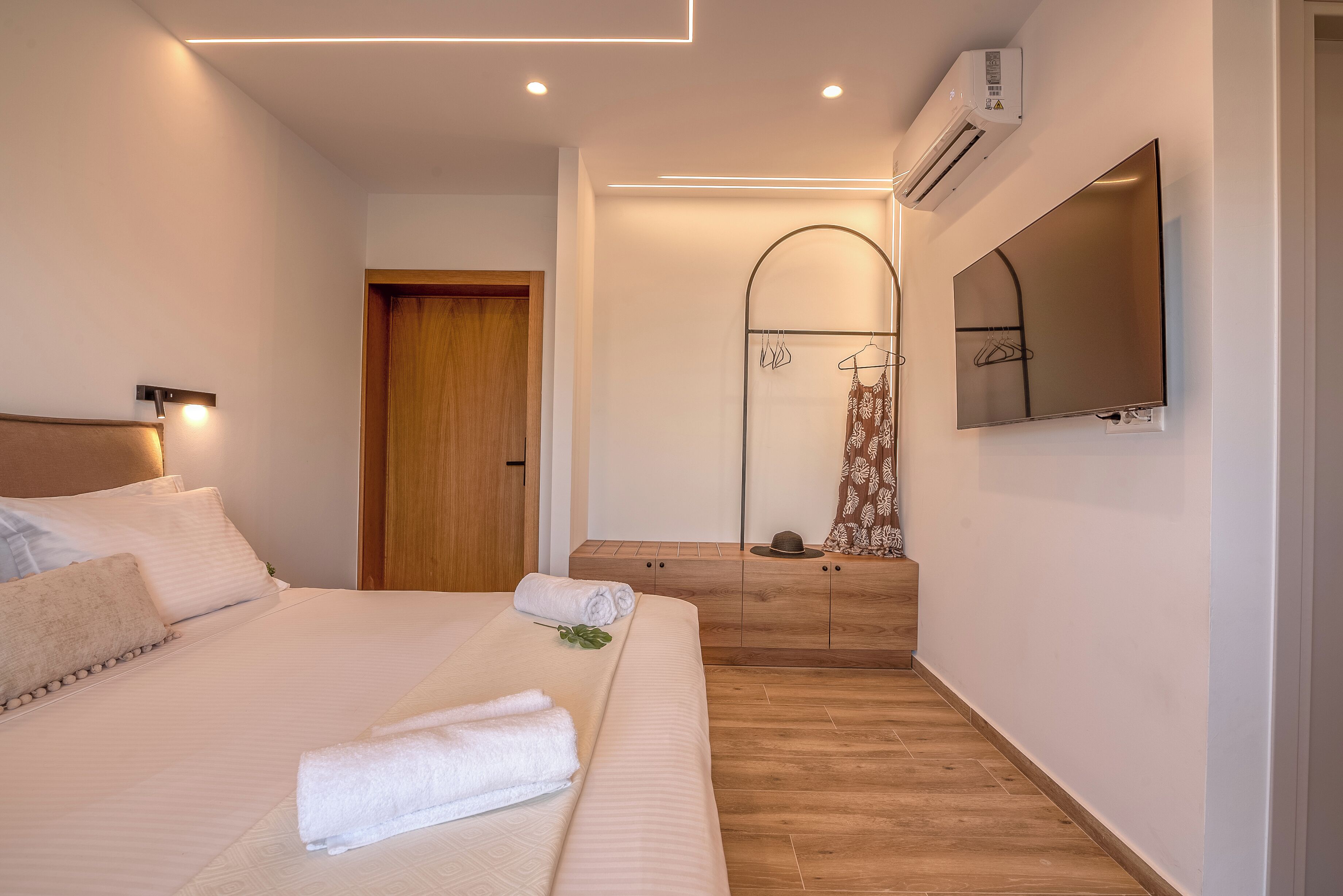 Una habitación de hotel moderna con una cama bien hecha, un armario de madera, un espejo y un televisor montado.
