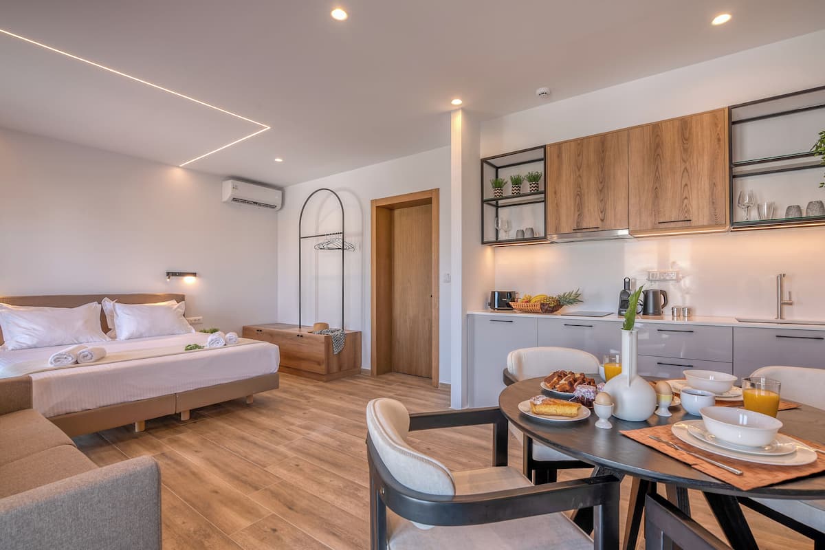 A modern hotel room with a bed, a dining area with breakfast, and a kitchen.
