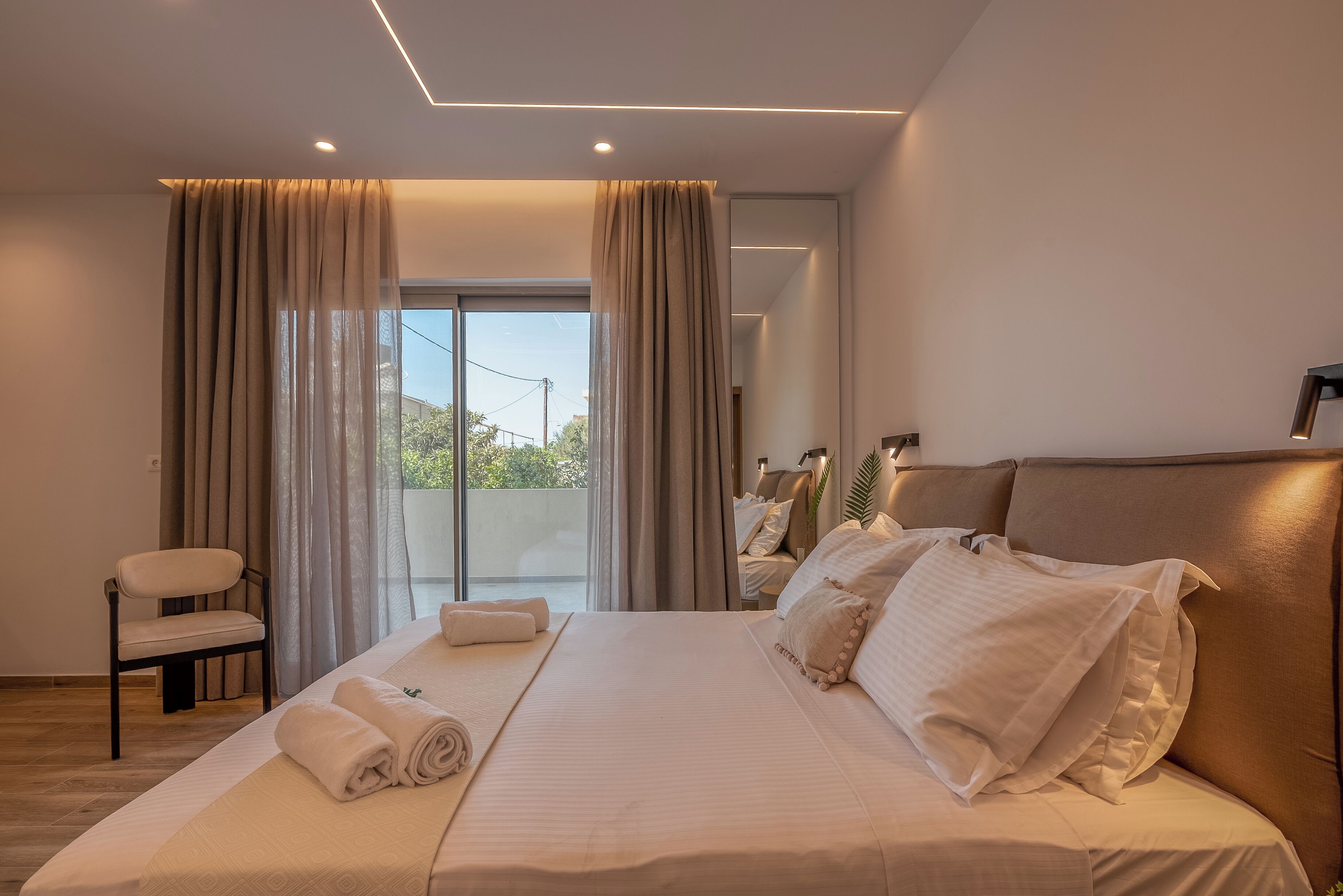 A modern hotel room with a large bed, a chair, and a view of the outdoors.