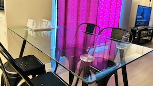 Et moderne hotelværelse med et glas spisebord, sorte stole og en pink gardin med et cirkelmønster.