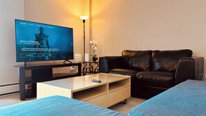 En moderne stue med et fladskærms TV, en lædersofa, et træsofabord og et lille sidebord med en lampe.