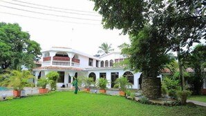A two-story building with a white facade, multiple balconies, and a well-maintained garden with various plants. - Pontoon Residence & Suites (Mombasa)