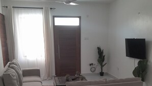 A living room with a sofa, a coffee table, a TV, and a ceiling fan. - Pontoon Residence & Suites (Mombasa)