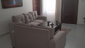 A living room with a beige sofa, a coffee table, and a painting on the wall. - Pontoon Residence & Suites (Mombasa)