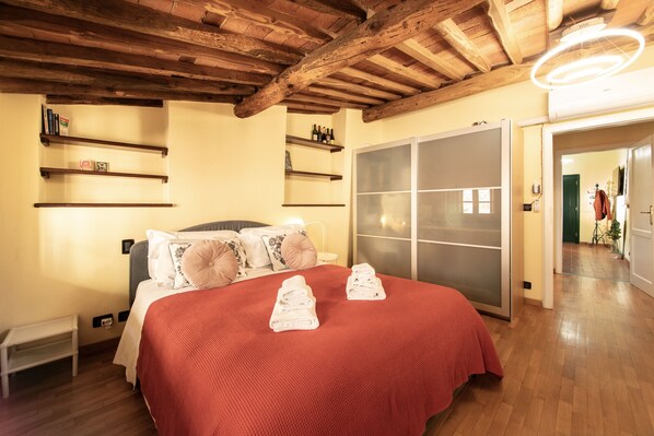 A bedroom with a wooden ceiling, a bed with a red bedspread, two towels on the bed, and a sliding glass door closet.