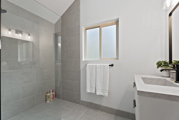 A modern bathroom with a glass shower enclosure, a white towel hanging on a door, and a sink with a potted plant.