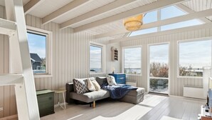 Una habitación amplia con techo alto, ventanas grandes y un rincón de descanso acogedor con sofá y mesita auxiliar.