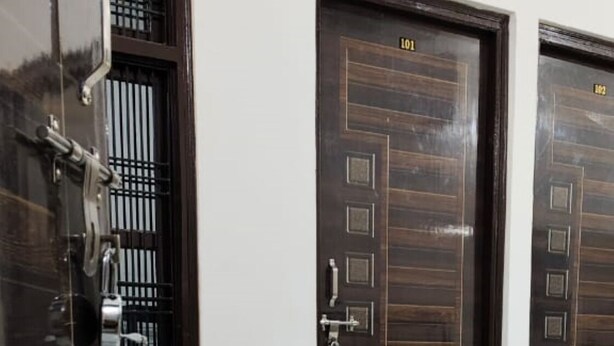 A room with a marble floor, a chair, and two dark wooden doors with numbers 101 and 102. - Bharat Raj Homestay By GRB (Faizabad)