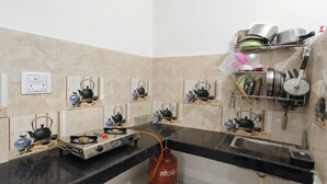 A kitchen with multiple gas stoves, shelves with teapots, and a gas cylinder. - Bharat Raj Homestay By GRB (Faizabad)