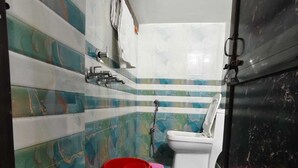 A bathroom with a toilet, a red bucket, and a shower area. - Bharat Raj Homestay By GRB (Faizabad)