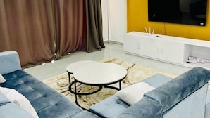 Een moderne woonkamer met een modulaire bank, een ronde salontafel en een flatscreen televisie bevestigd aan een gele muur.