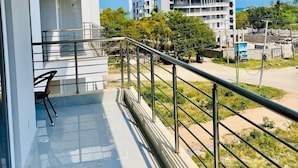 Een balkon met een stoel, een leuning en uitzicht op gebouwen en groen.
