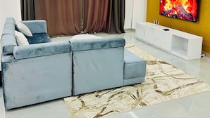 Een moderne woonkamer met een hoekbank, een flatscreen-tv, een plafondventilator en een decoratief vloerkleed.