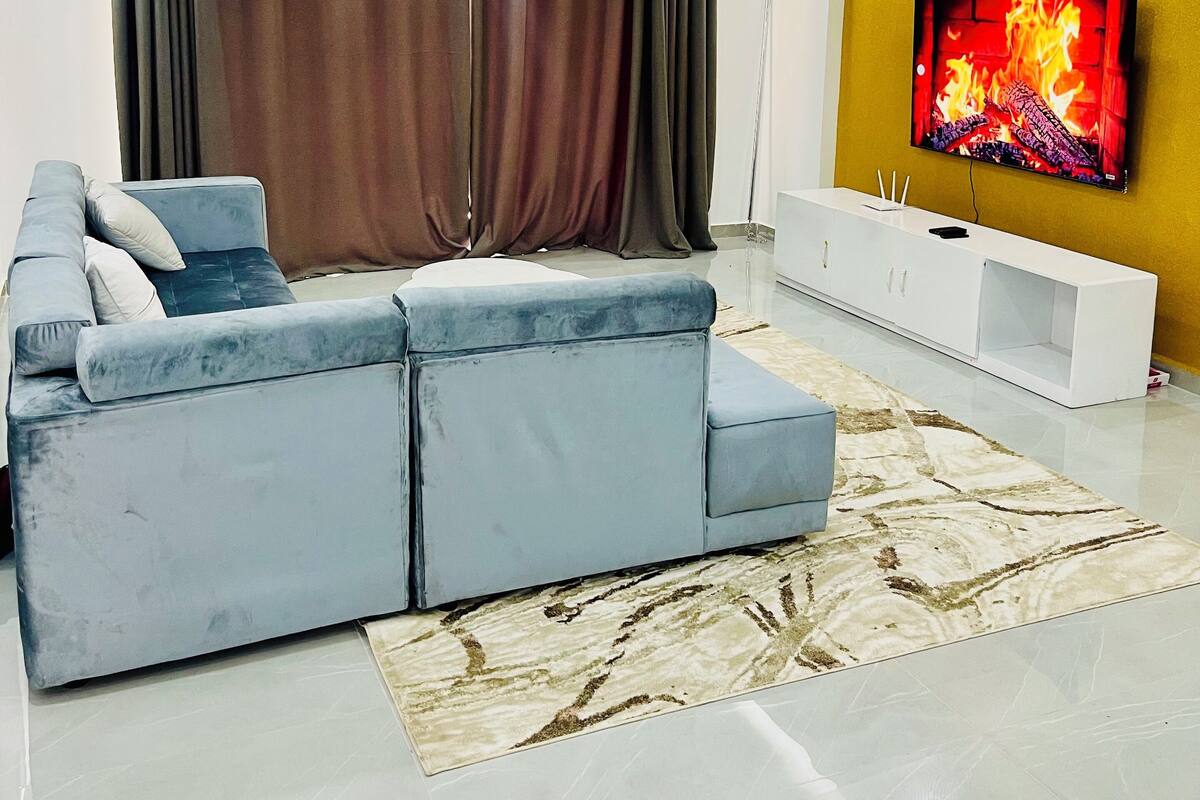 A modern living room with a sectional sofa, a flat-screen TV, a ceiling fan, and a decorative rug.