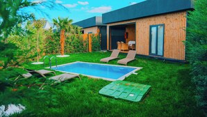 Ein modernes Haus mit Swimmingpool, zwei Liegestühlen und einem grünen Rasen.