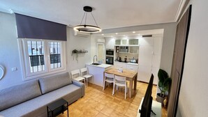 A compact living space with a sofa, a dining table with chairs, a kitchen area with cabinets and appliances, and a small TV.