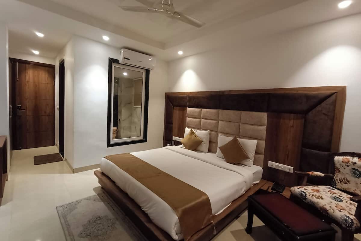 A modern bedroom with a large bed, a wooden headboard, a bench, a chair, a mirror, and an air conditioning unit.