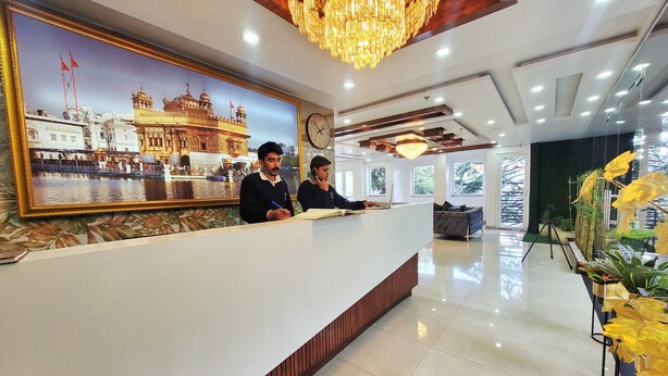 Een hotel receptie met een groot ingelijst beeld van een historisch gebouw, een moderne kroonluchter en een receptiebalie.