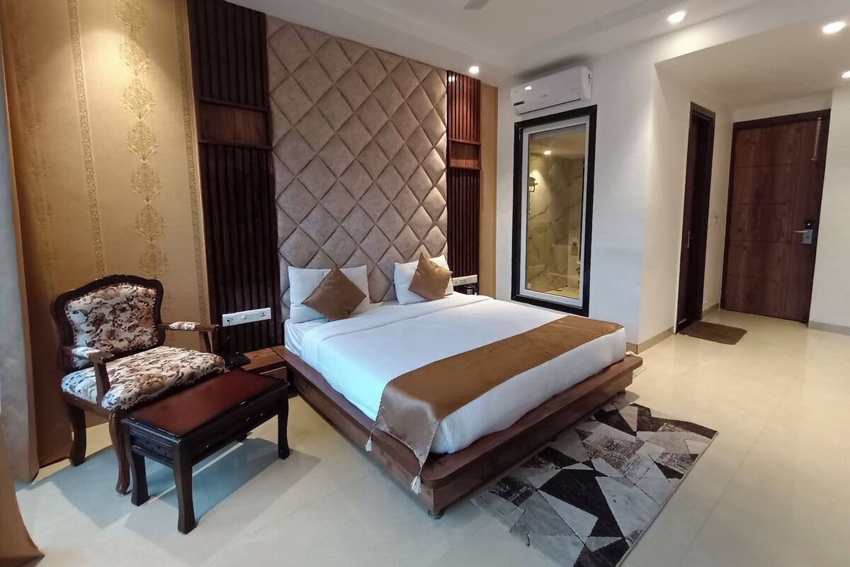 A modern hotel room with a large bed, a wooden nightstand, a chair, and a glass-enclosed shower.