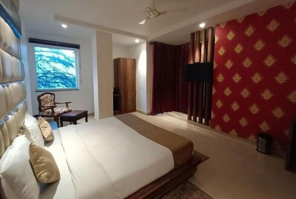 A hotel room with a large bed, a TV, a window with a view, and a red patterned wall. - RR HOTEL BY SONACHI (Dharamshala)