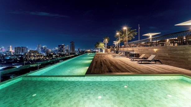 A rooftop infinity pool with a wooden deck, lounge chairs, and city skyline views. - The Skye Phnom Penh Hotel & Apartments (Phnom Penh)