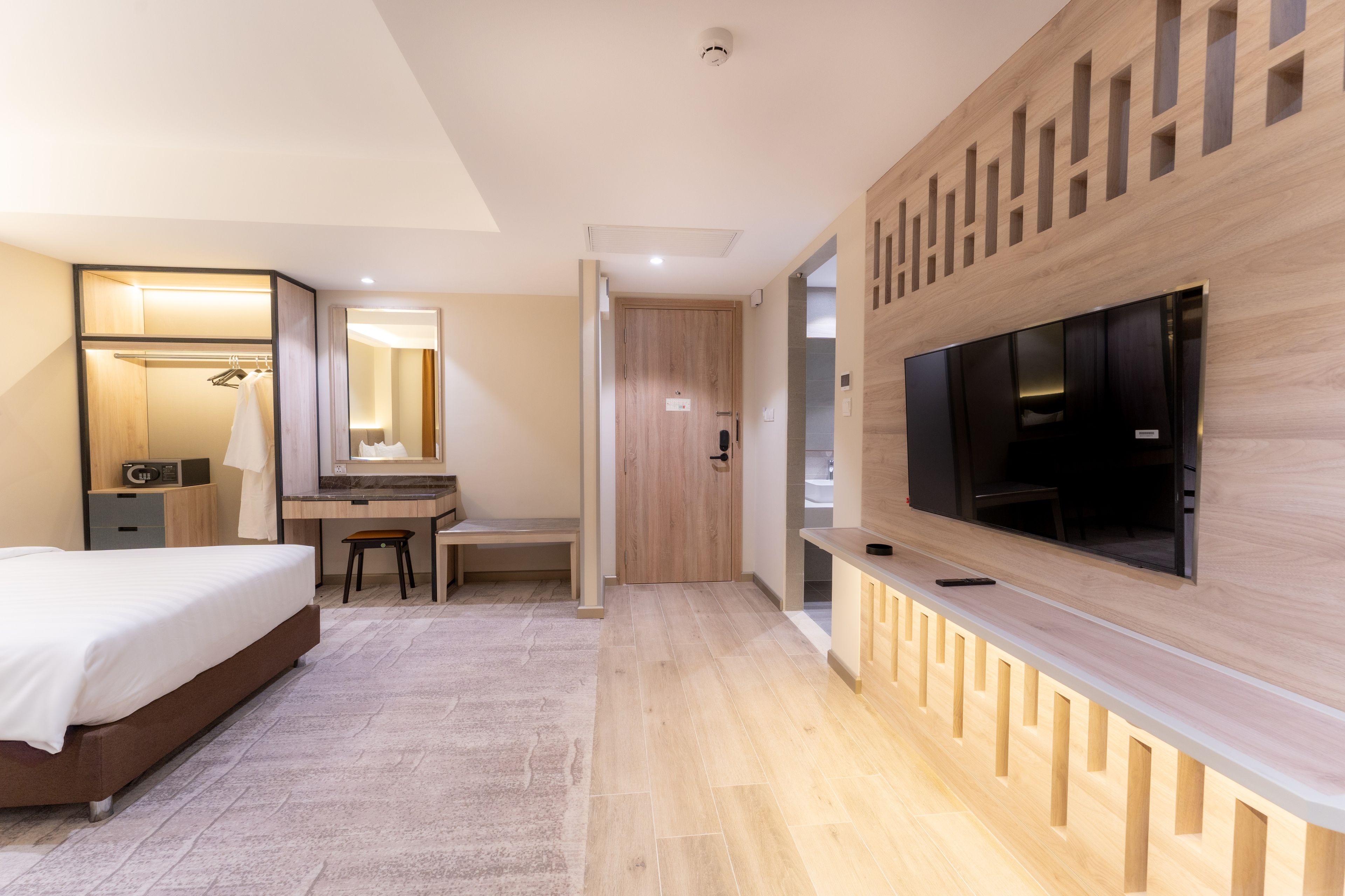 Une chambre d’hôtel moderne équipée d’un lit, d’un bureau, d’une chaise et d’un grand téléviseur fixé au mur.