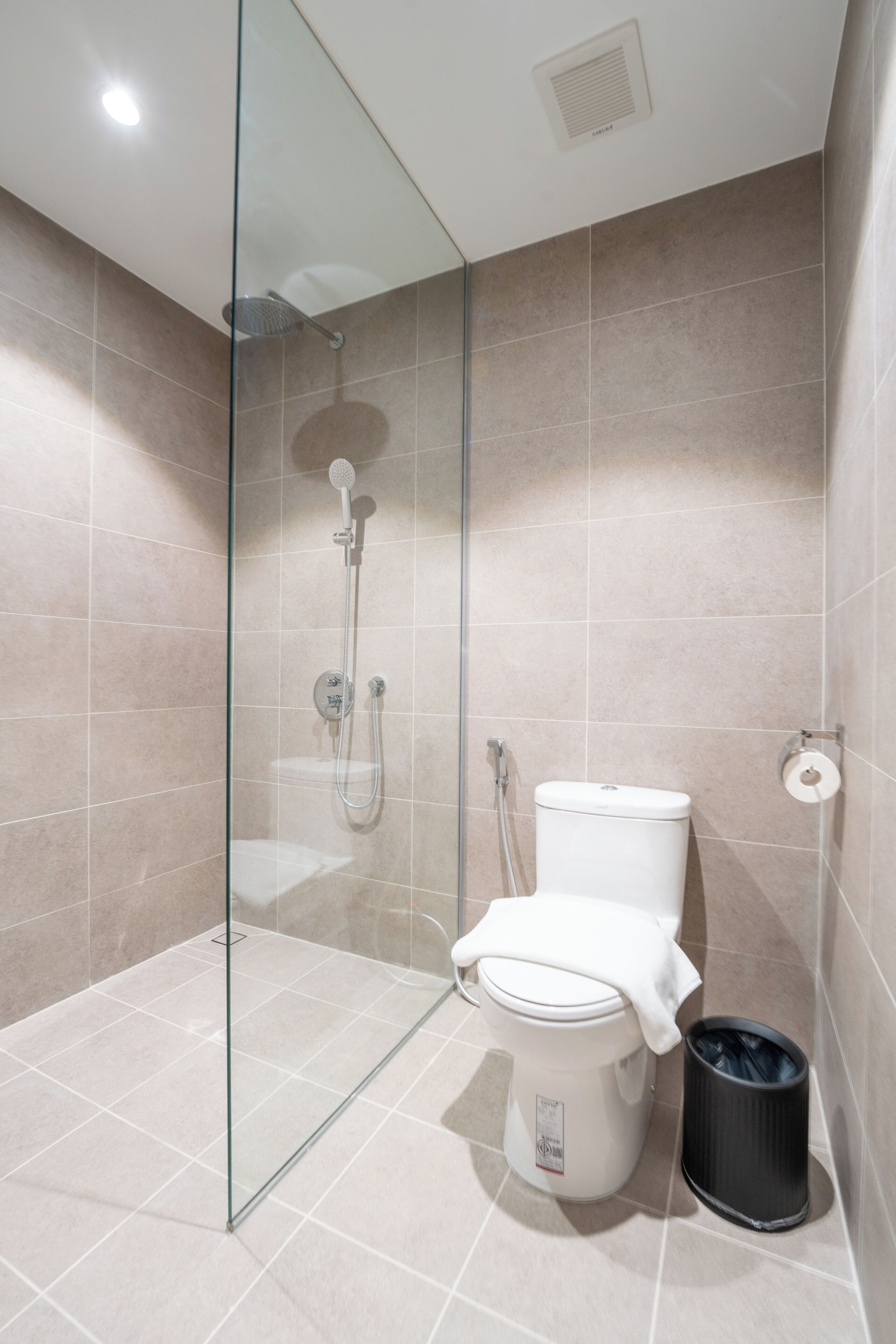 A modern bathroom with a glass-enclosed shower, a toilet, and a trash bin.