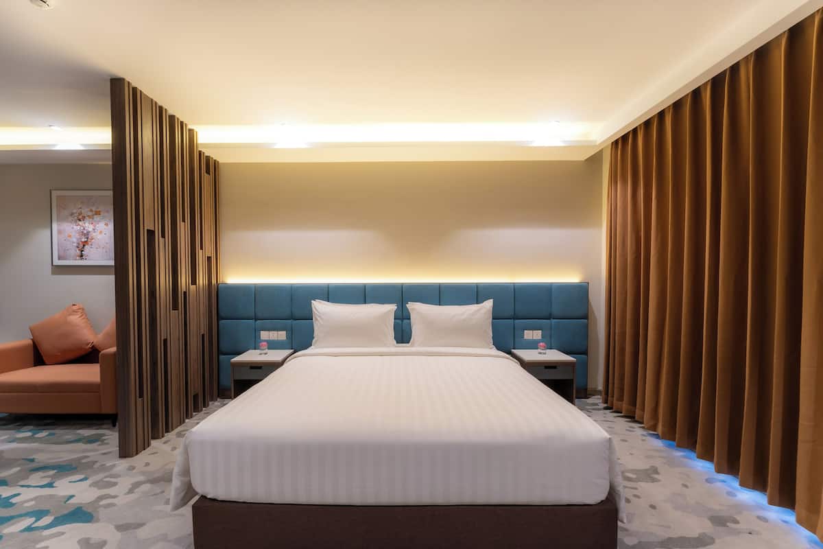 Ein Hotelzimmer mit einem großen Bett, einem blauen Kopfteil, einem Nachttisch, einem Beistelltisch, einem Sofa und einem Vorhang.