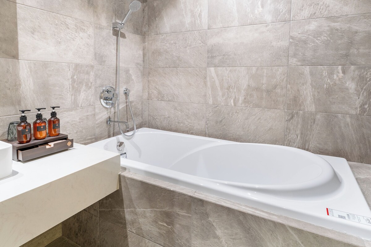 Een moderne badkamer met een vrijstaand bad, een douchekop en een wastafel met toiletartikelen.