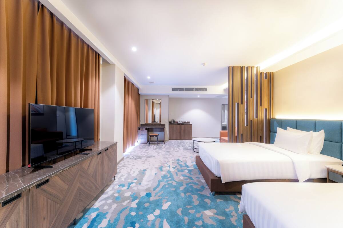 Ein Hotelzimmer mit Flachbildfernseher, zwei Betten, einem Schreibtisch und einem Badezimmer.