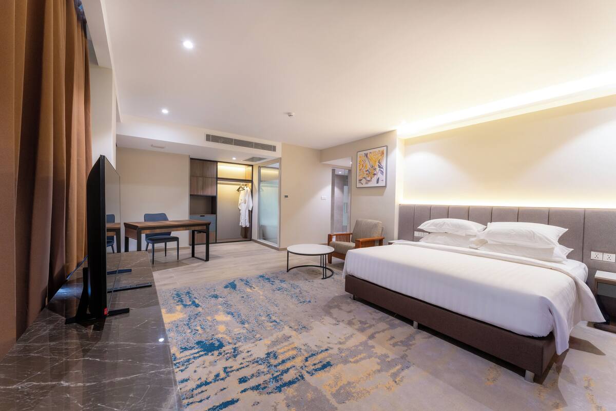Ein Hotelzimmer mit einem großen Bett, einem Schreibtisch mit Stuhl, einem kleinen runden Tisch und einem Fernseher.