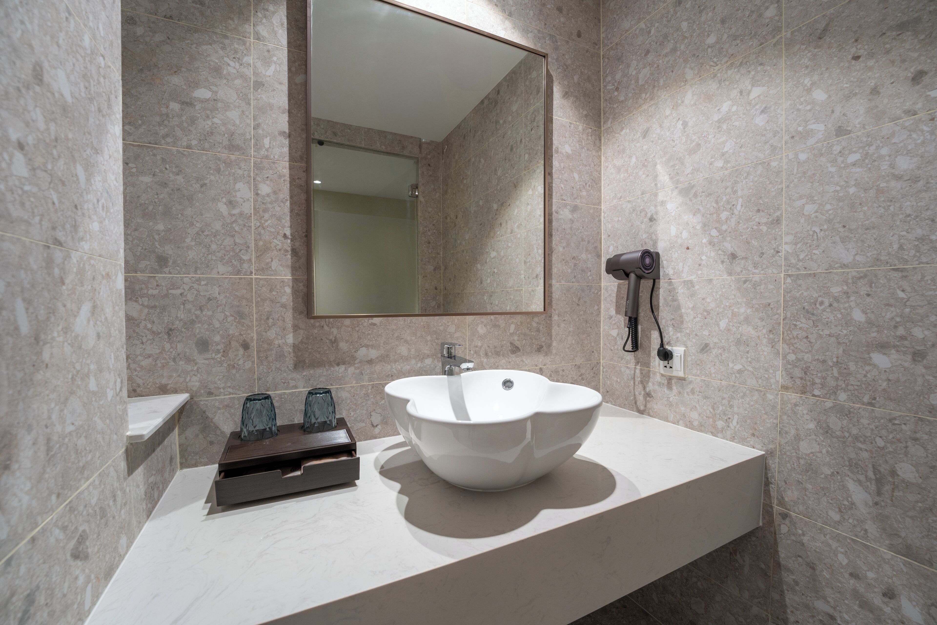 A modern bathroom with a white sink, a mirror, and a hairdryer mounted on the wall.