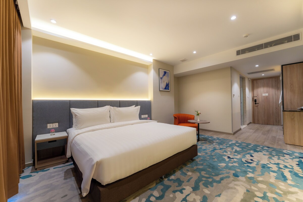 Een hotelkamer met een groot bed, een klein tafeltje, een oranje stoel en een houten garderobe.
