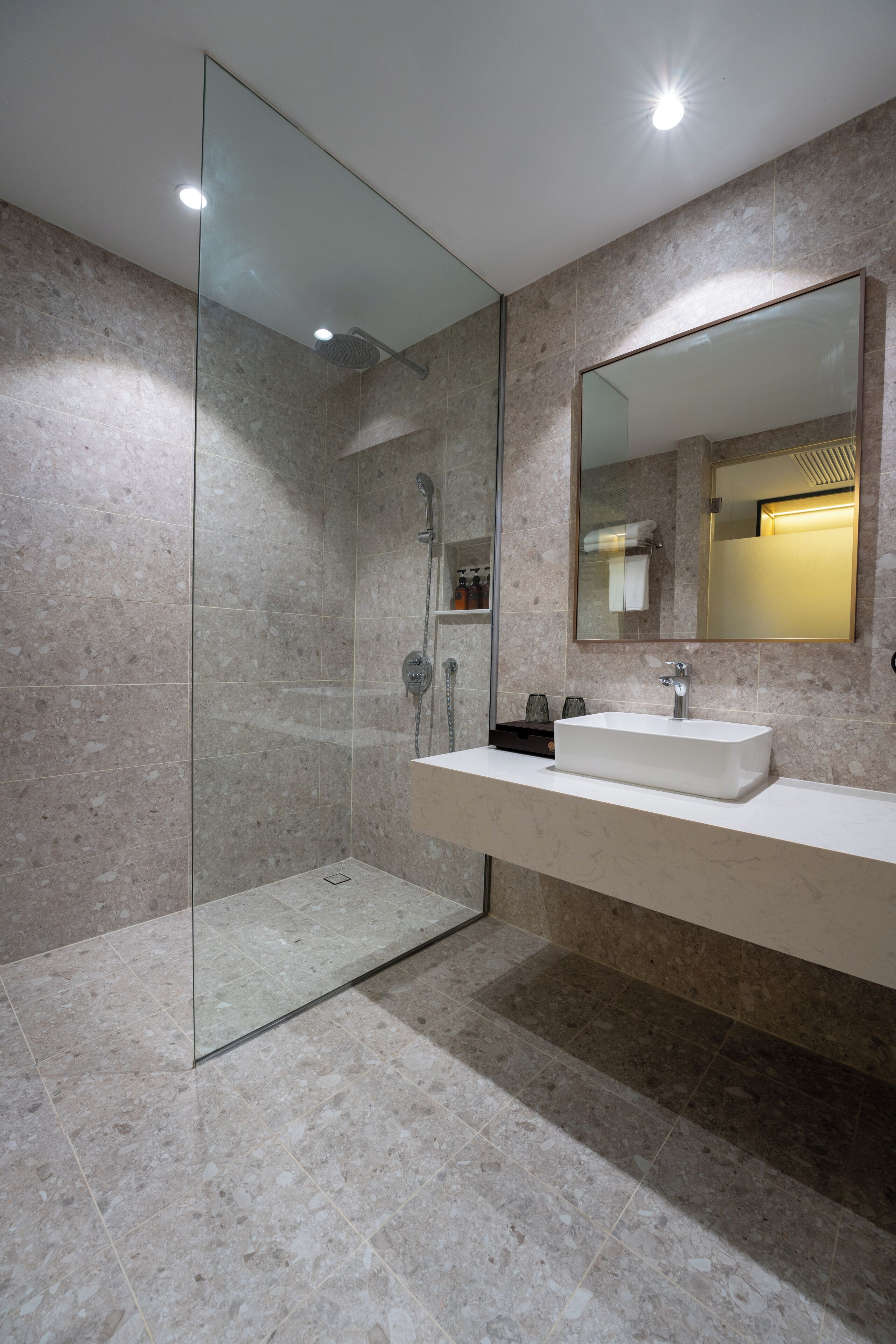 A modern bathroom with a glass-enclosed shower, a large mirror, and a marble-tiled floor.