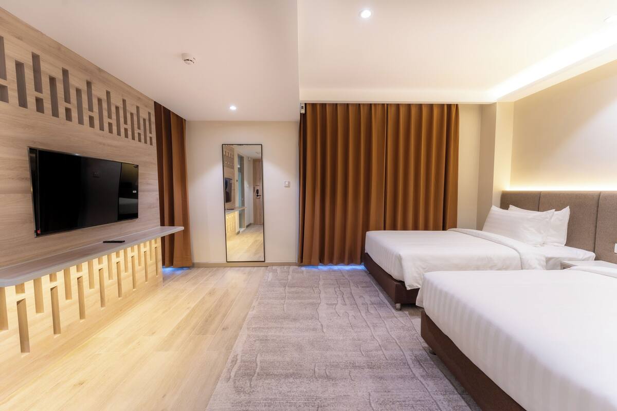 Ein modernes Hotelzimmer mit Flachbildfernseher, zwei Betten, einem großen Spiegel und einer Wand mit Holzverkleidung.