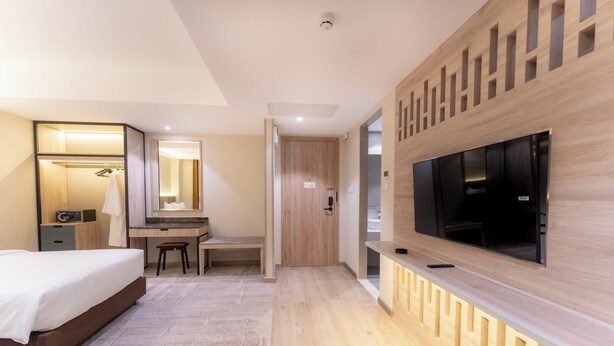 Une chambre d’hôtel moderne équipée d’un lit, d’un bureau, d’une chaise, d’une télévision et d’un dressing.